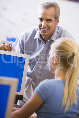 A teacher talks to a schoolgirl using a computer in a high schoo