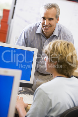 A teacher talks to a schoolboy using a computer in a high school