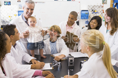 A science teacher with a baby surrounded by students in a high s