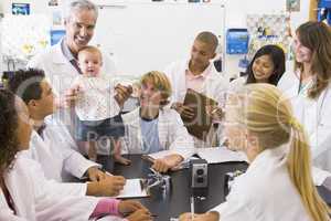 A science teacher with a baby surrounded by students in a high s