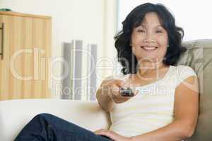 Woman sitting in living room holding remote control smiling