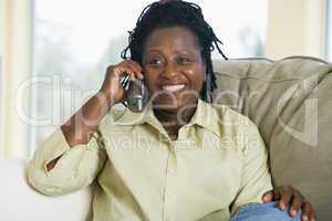 Woman sitting in living room using telephone and smiling