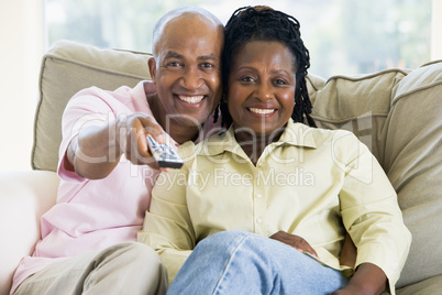 Couple relaxing in living room holding remote control and smilin