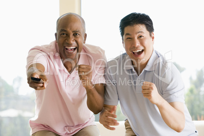 Two men in living room with remote control cheering and smiling