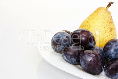 Yellow pear on a white plate with plums