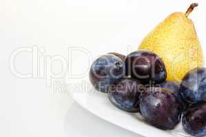 Yellow pear on a white plate with plums