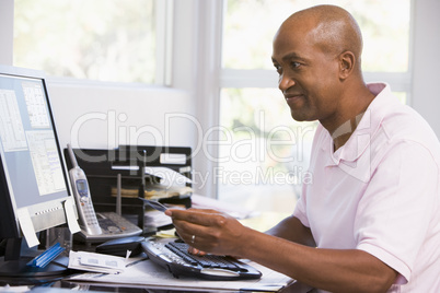 Man in home office using computer holding credit card and smilin