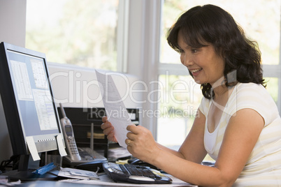 Woman in home office with computer and paperwork smiling