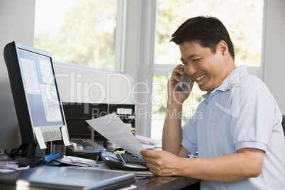 Man in home office with computer and paperwork on telephone smil