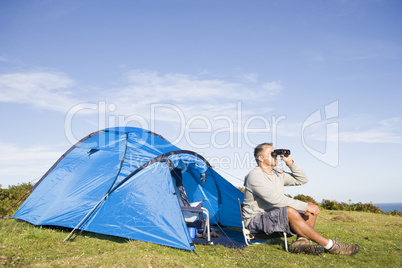 Man camping outdoors and looking through binoculars