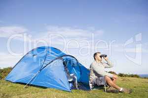 Man camping outdoors and looking through binoculars