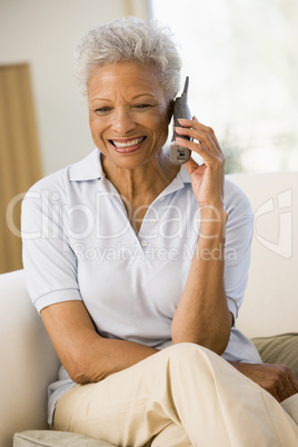 Woman sitting in living room using telephone and smiling