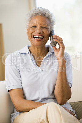 Woman sitting in living room using telephone and smiling