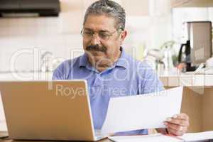 Man in kitchen with laptop and paperwork
