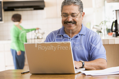 Man in kitchen with laptop smiling with woman in background
