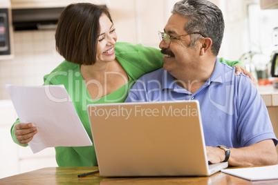 Couple in kitchen with laptop and paperwork smiling