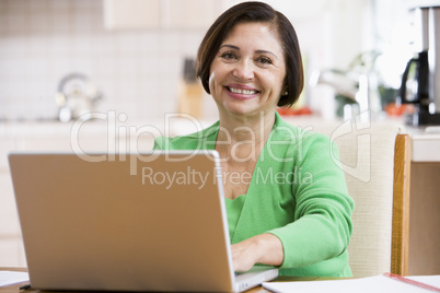 Woman in kitchen with laptop smiling