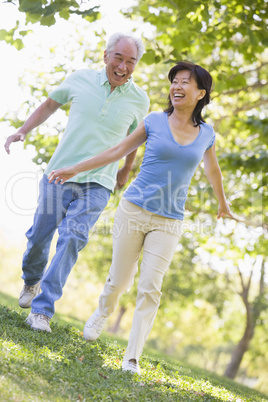 Couple running outdoors in park by lake smiling