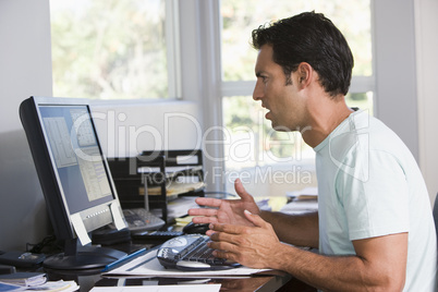 Man in home office using computer looking frustrated