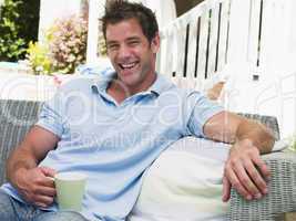 Man sitting on patio with coffee laughing