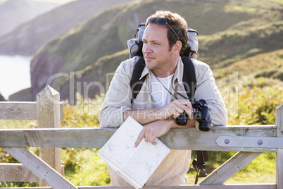 Man relaxing on cliffside path holding map and binoculars