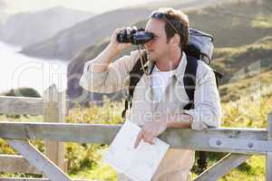 Man relaxing on cliffside path holding map and binoculars