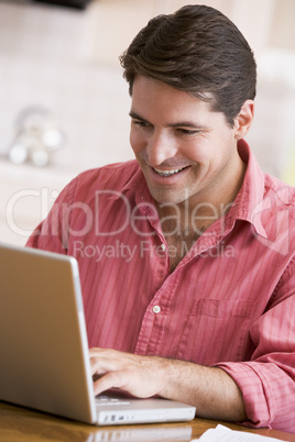 Man in kitchen using laptop smiling