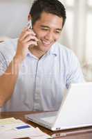 Man in dining room on cellular phone using laptop smiling