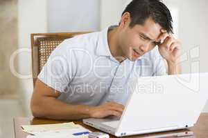 Man in dining room using laptop and frowning