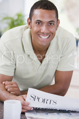 Man in kitchen reading newspaper and smiling