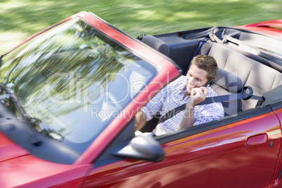Man driving convertible car using cellular phone and smiling
