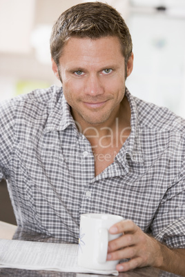 Man in kitchen reading newspaper and smiling