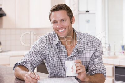 Man in kitchen reading newspaper and smiling