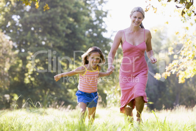 Woman and young girl running outdoors holding hands and smiling