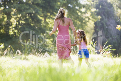 Woman and young girl running outdoors holding hands and smiling