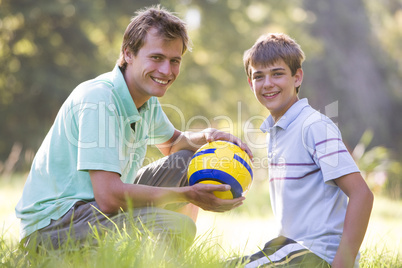 Man and young boy outdoors with soccer ball smiling