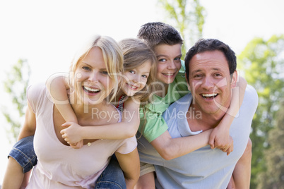 Couple giving two young children piggyback rides smiling