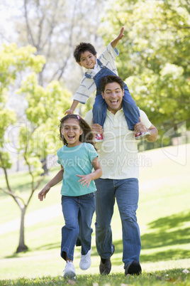 Man with two young children running outdoors smiling