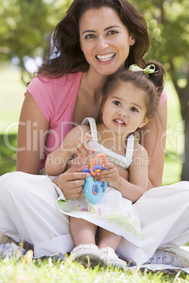 Woman and young girl sitting outdoors with toy smiling