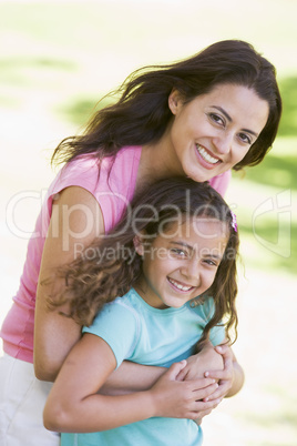 Woman and young girl outdoors embracing and smiling