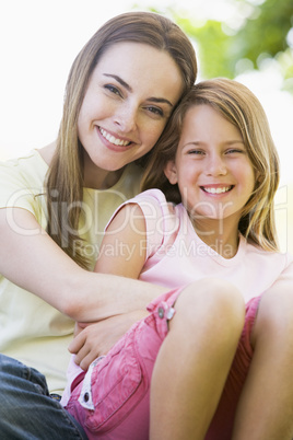 Woman and young girl outdoors embracing and smiling