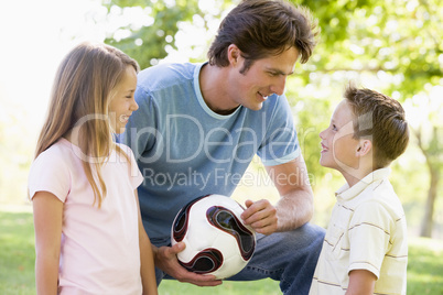 Man and two young children outdoors holding volleyball and smili