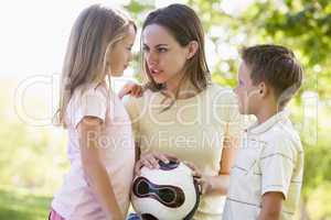 Woman and two young children outdoors holding volleyball and smi