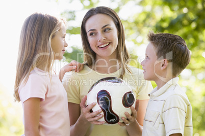 Woman and two young children outdoors holding volleyball and smi