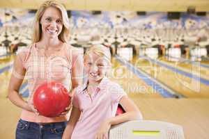 Woman and young girl in bowling alley holding ball and smiling
