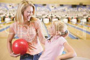 Woman and young girl in bowling alley holding ball and smiling