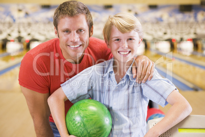 Man and young boy in bowling alley holding ball and smiling
