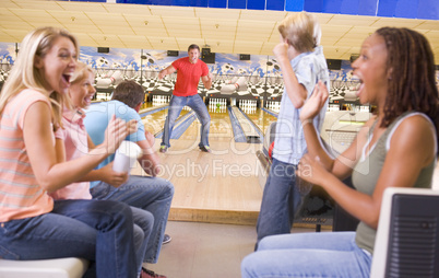 Family in bowling alley with two friends cheering and smiling