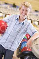 Young boy in bowling alley holding ball and smiling