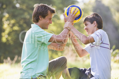 Man and young boy outdoors holding soccer ball and smiling